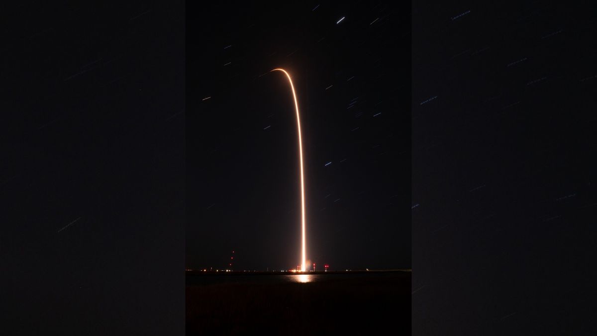 a black-and-white rocket launches at night above a bright plume of fire