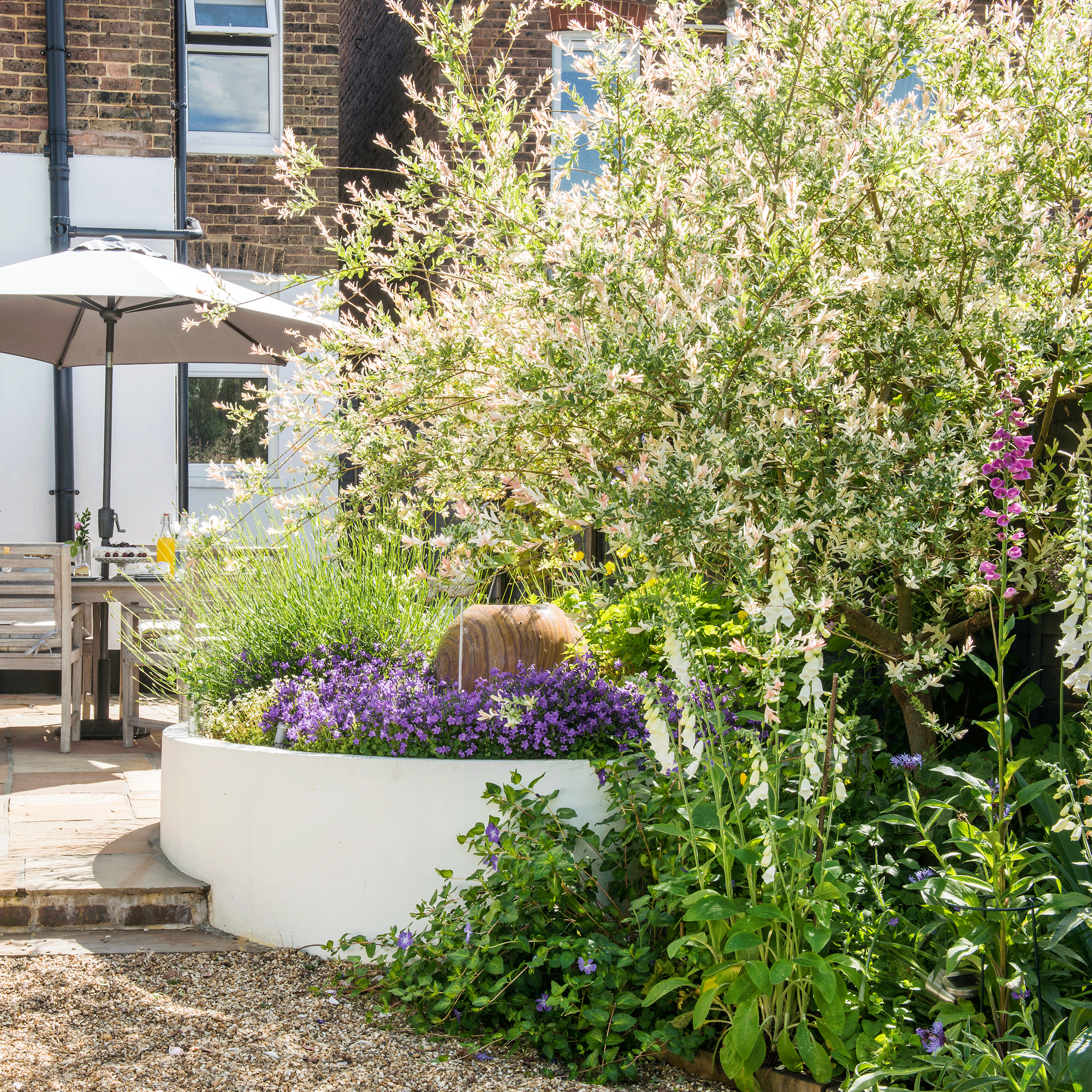 a garden with round raised beds and a raised patio area with a table and chairs and parasol
