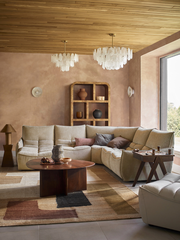 Image of a beige L-shaped sectional in a pink limewash room with a blush pink rug and a wooden coffee table.