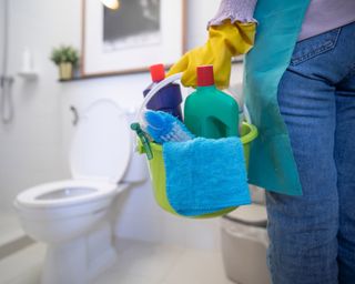 Lady holding bucket of cleaning supplies in front of a toilet
