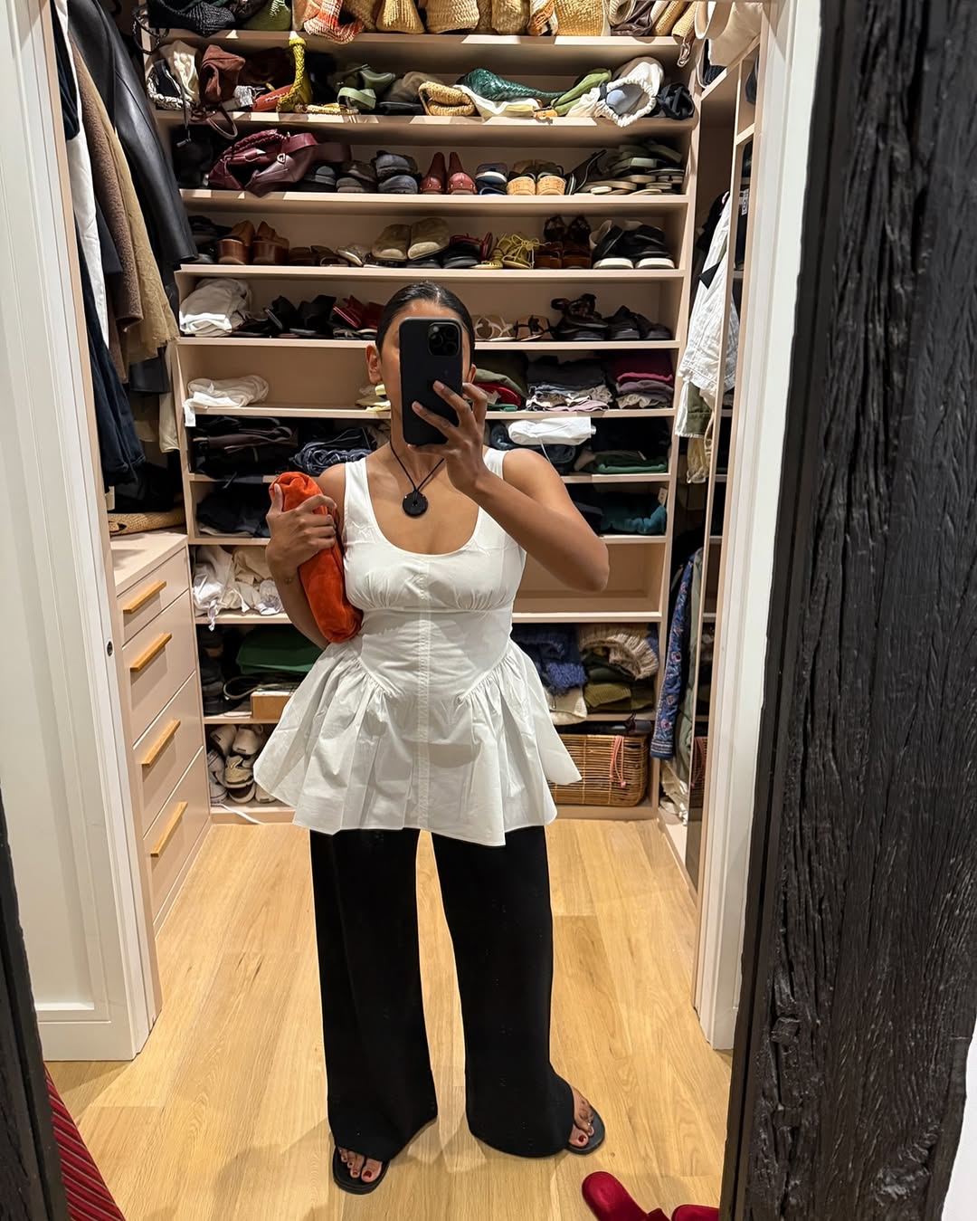 Monikh in a closet holding an orange clutch