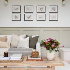 A neutral-coloured small living room with a dado rail and a botanical gallery wall above the cream sofa