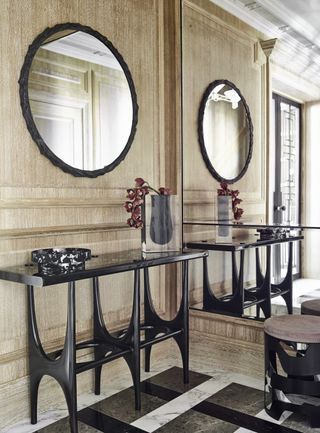 entryway with wooden panels, black console, black mirror, mirror wall, marble floor