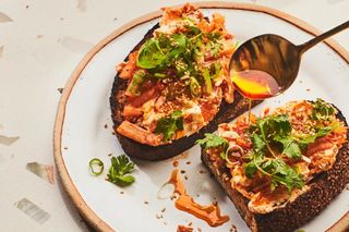 kimchi mounded on toast with a gold spoon adding chile oil