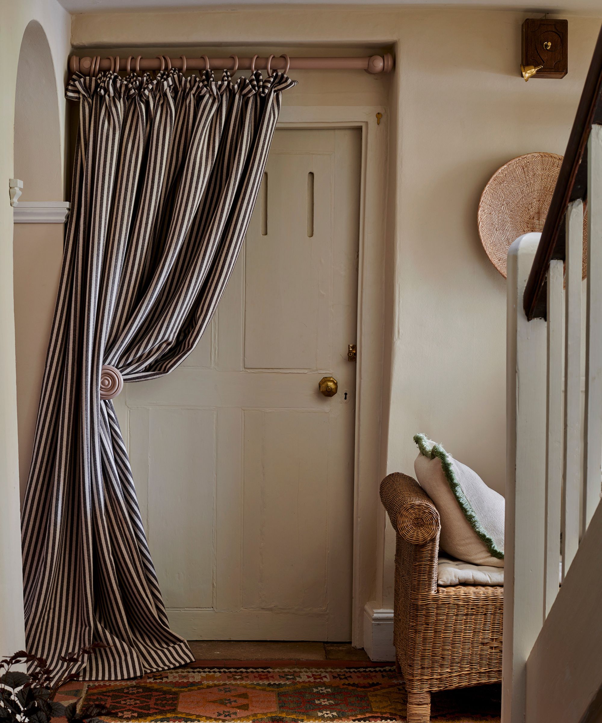 Front door with striped door curtain, persian rug on floor and rattan bench