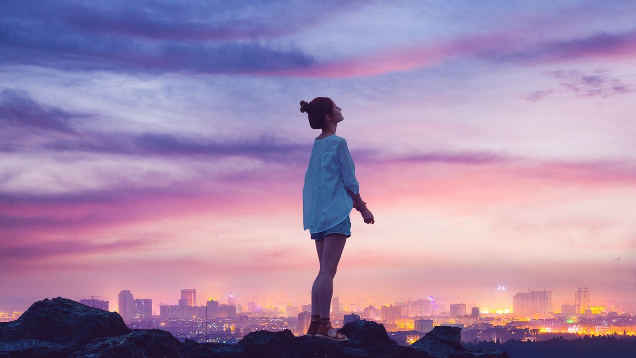 woman on rock looking into the sky as city is below