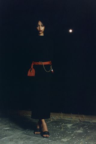 Woman stands in dark in black dress with belt