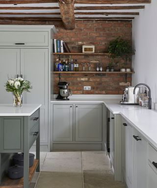A grey kitchen with white worktops and a bare brick wall