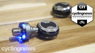 A pair of Wahoo Powrlink Zero pedals on a table, with the blue light illuminated and a 'recommends' badge overlaid