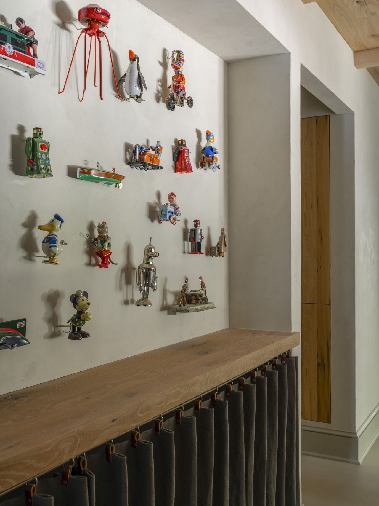 Close-up image of an off-white wall with vintage toys hung on it. There is a wooden shelf on the wall.