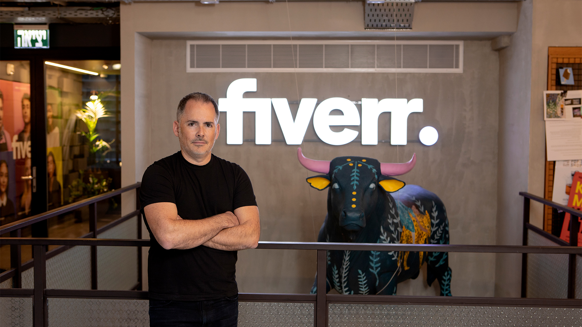 Fiverr CEO Micha Kaufman pictured standing in front of the company&#039;s logo and branding at its head office.