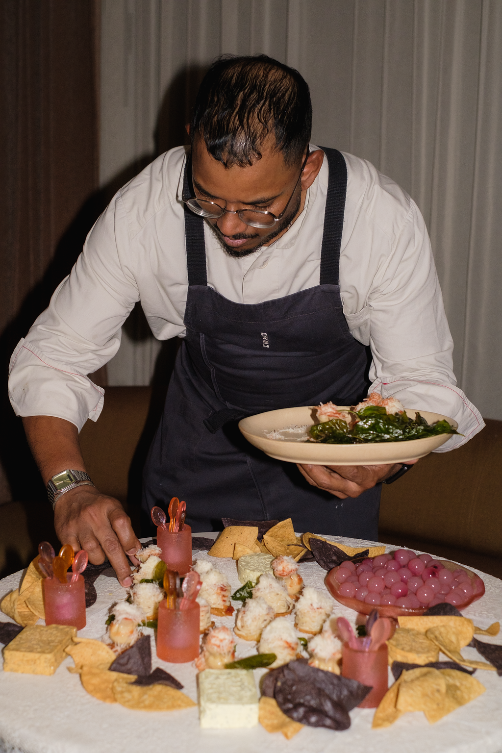 Event pictures showing a crowd mingling, eating food, and sipping drinks at a beautifully decorated bar with velvety surfaces, sculptural decor, and colorful bites.