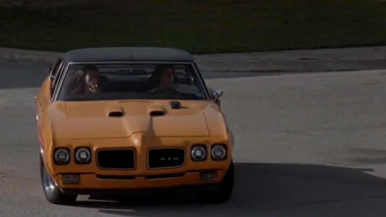 A yellow pontiac driving through a parking lot.