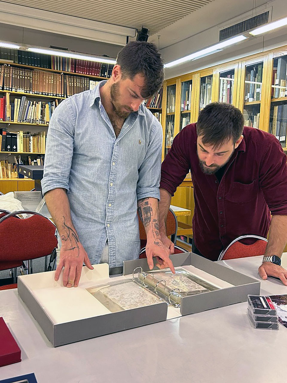 two young bearded men examine a notebook on a table in a library