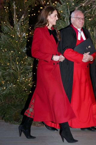 Princess Kate arrives at her annual holiday carol service wearing a red bow topped coat with black boots and a tartan dress