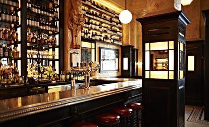 Balthazar restaurant with dark wood bar and brass counter, red leather bar stools and ochre colored walls