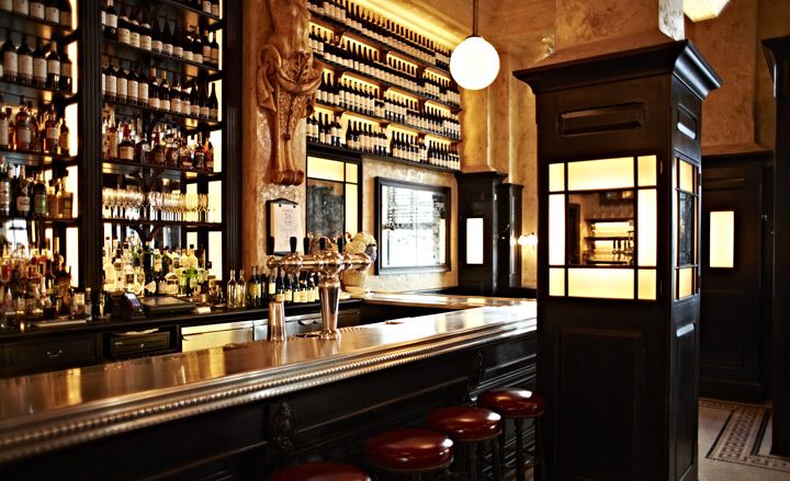 Balthazar restaurant with dark wood bar and brass counter, red leather bar stools and dim lighting