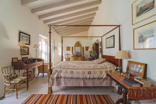 Bedroom with simple wooden four poster bed striped rug ornate mirror painted ceiling beams
