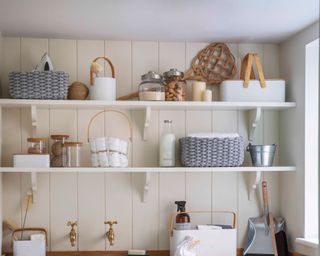 open shelving against wood panelling with grey baskets, white containers and glass jars in a laundry room