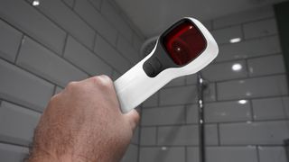 Holding a Jepwco G6 Sport hidden camera detector to spot a hidden camera lens in a shower with the glint of a lens visible in the viewfinder