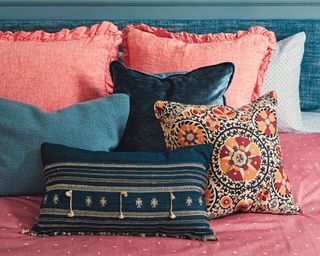 Lots of pillows arranged nicely on a pink bedding in a blue and pink styled bedroom