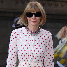 Anna Wintour wears oversize sunglasses and a red and white polka dot dress