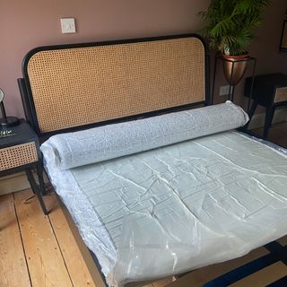 The Zinus Green Tea Memory Foam mattress being tested in a bedroom with a rattan headboard and pink walls