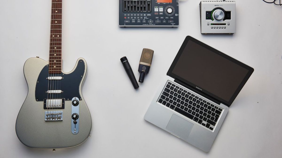 A top down shot of a laptop, electric guitar, microphone, and audio interface on a white floor