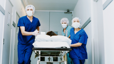 Three surgeons in surgical scrubs push a patient on a trolley down a hospital corridor.