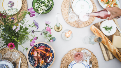 An outdoor table covered in tablescaping accessories, such as a blue table runner, blooms, and glassware