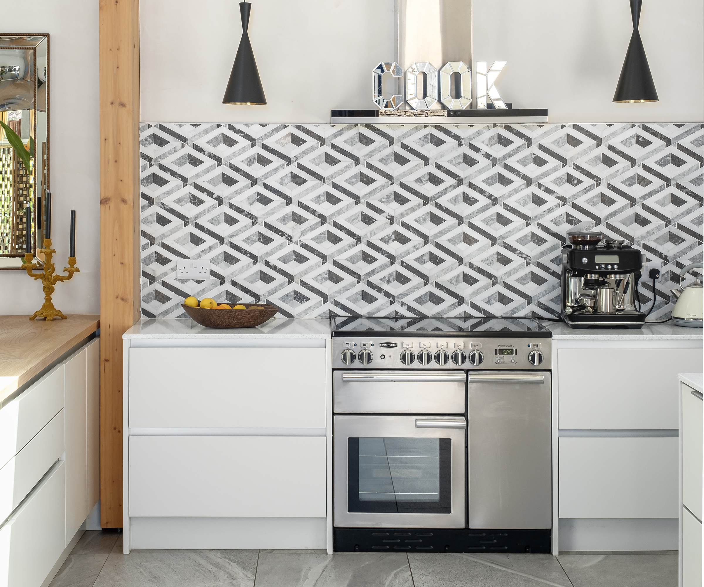 A kitchen with abstract tiling as the splashback and white cabinets with a stainless steel oven and extractor
