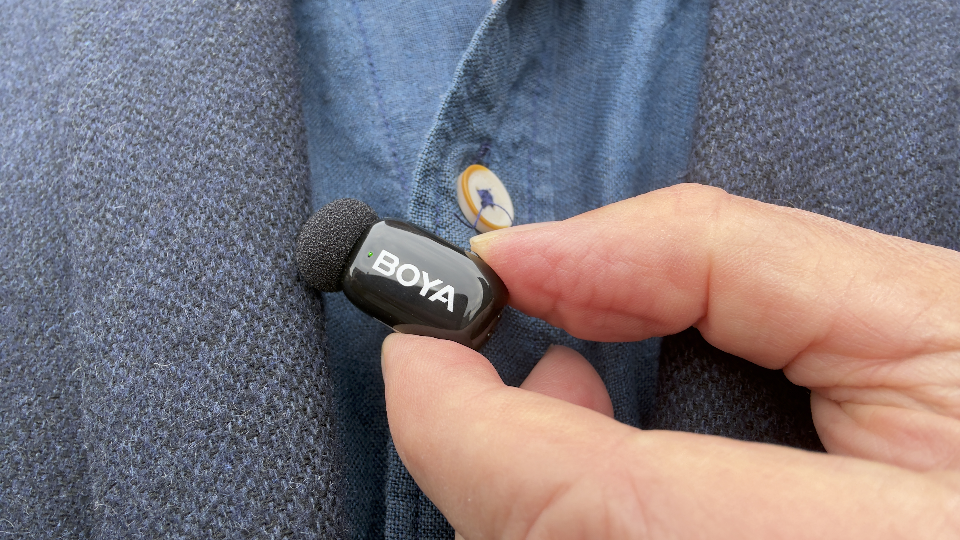 Close-up of the Boya mini 2 microphone clipped to a shirt. The status light shines green, indicating that noise-cancellation is active