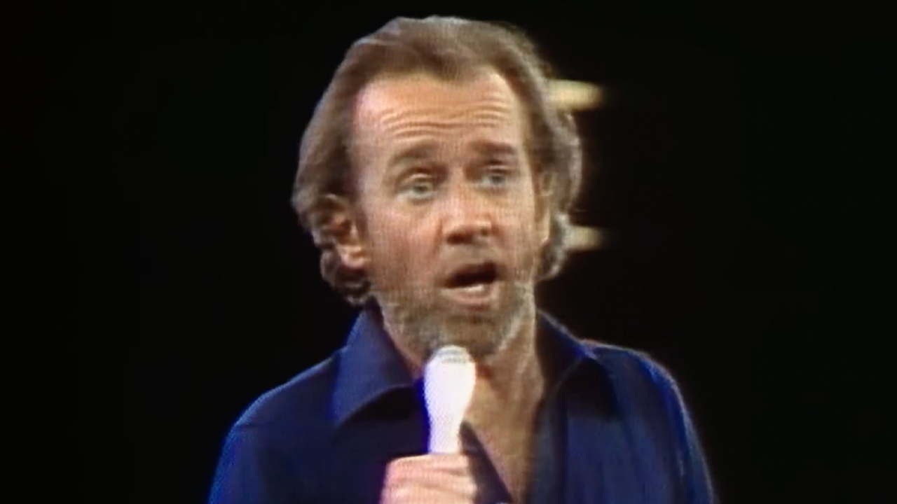 George Carlin, with long hair and a blue button up, performing standup, Archival footage used in HBO's doc George Carlin's American Dream.