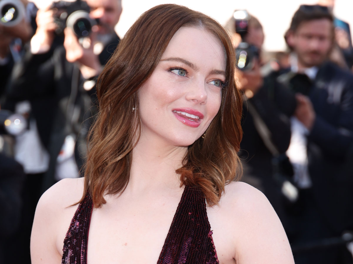 Emma Stone looks away from the camera wearing a plunging maroon dress