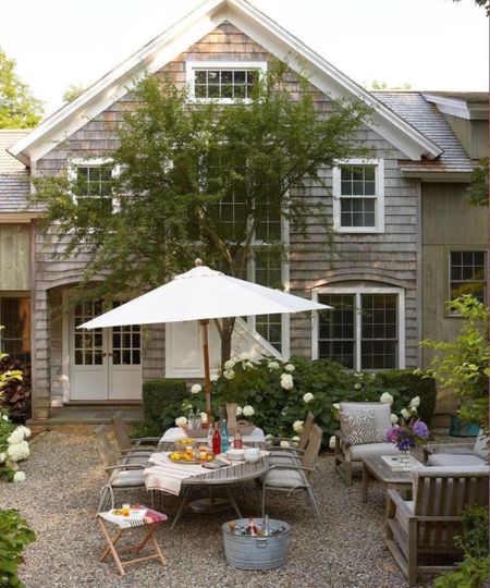 hamptons home with a shingle patio area surrounded by hydrangeas with a dining table and patio umbrella laid for lunch