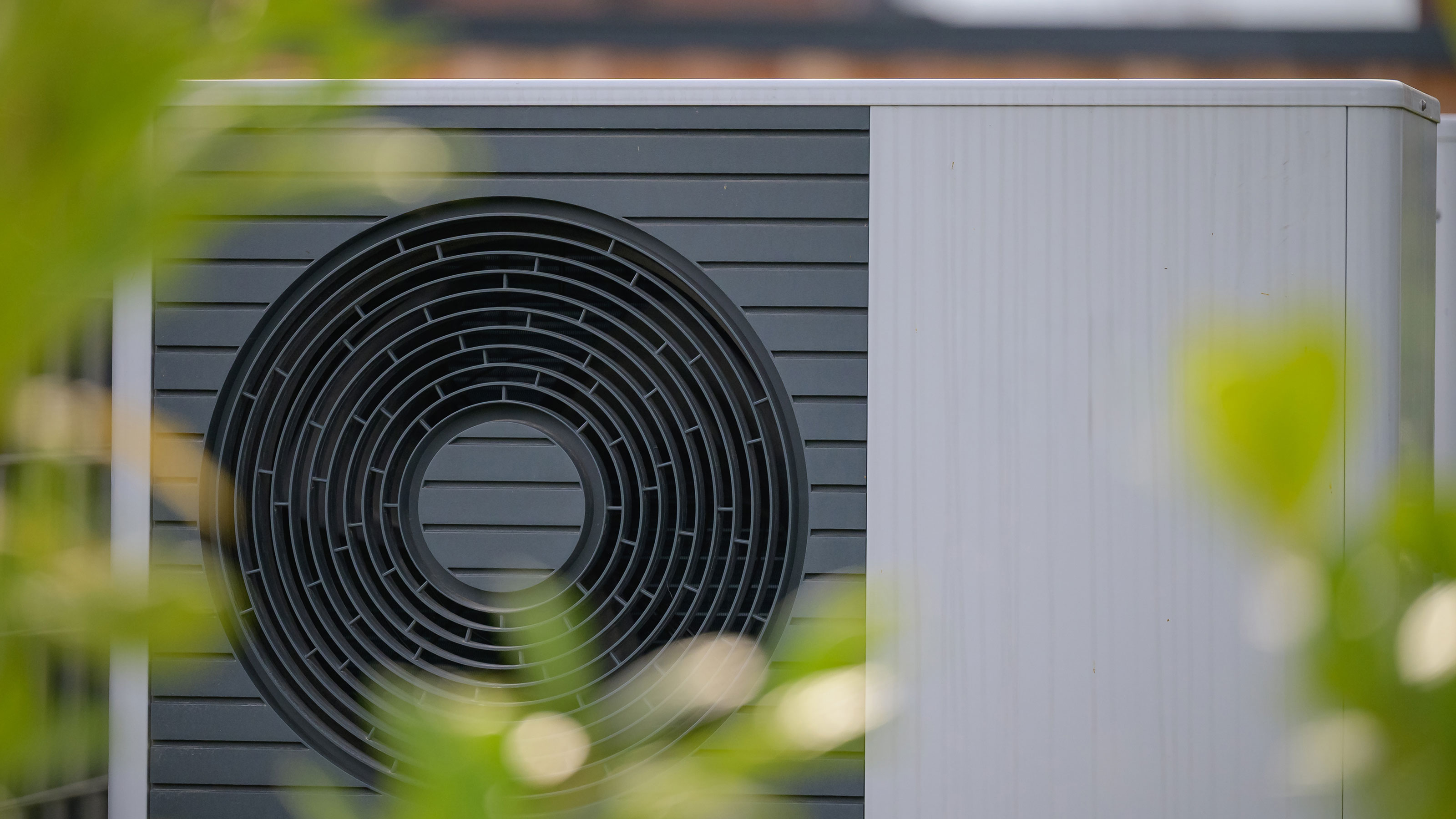 Heat pump in front of brick wall with blurred foliage in foreground