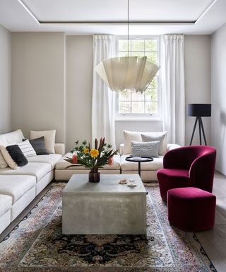 A minimalist living room with white walls, a white pendant light and a red velvet armchair
