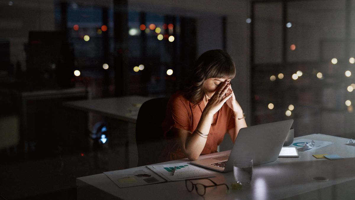 A woman sitting by her desk at her workplace alone, head in hands