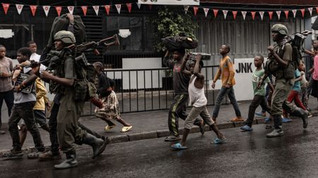 Members of the M23 armed group walk alongside residents through a street in Goma