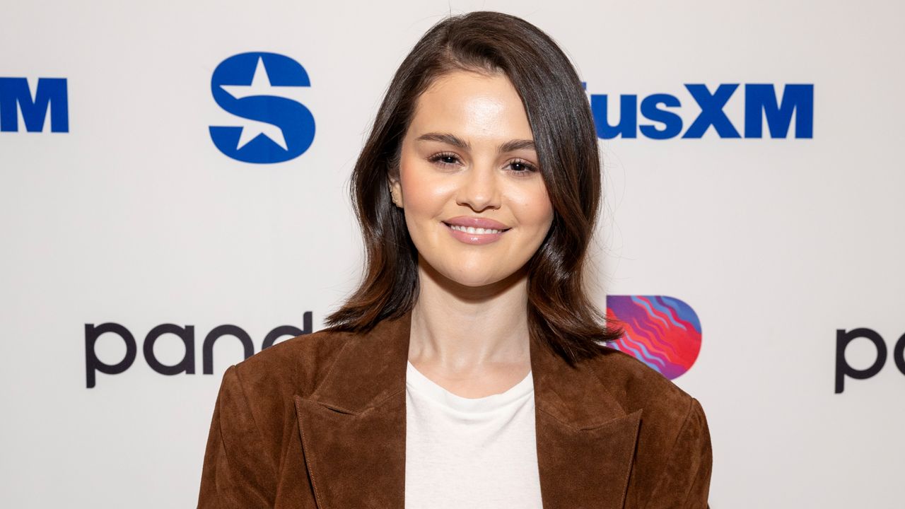 Selena Gomez wearing a suede trench coat and a white T-shirt on a red carpet