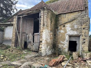 A stone barn with two dilapidated front timber doors