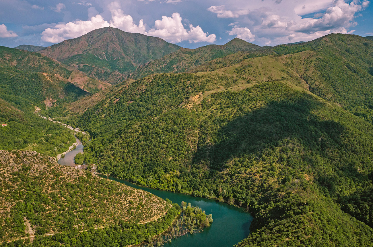 A deep blue river running between green hilly terrain, with mountains in the background