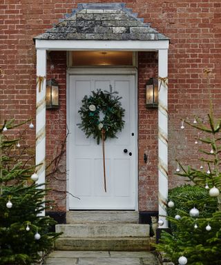 Traditional front door decorated with a wreath and two christmas trees either side of the porch