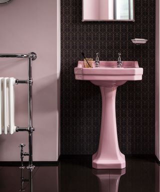 A pink and chrome bathroom with black and gold statement wallpaper, mirror and radiator with black shiny tiles