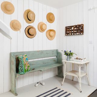 entrance hall with white wooden walls wooden bench and hats on walls