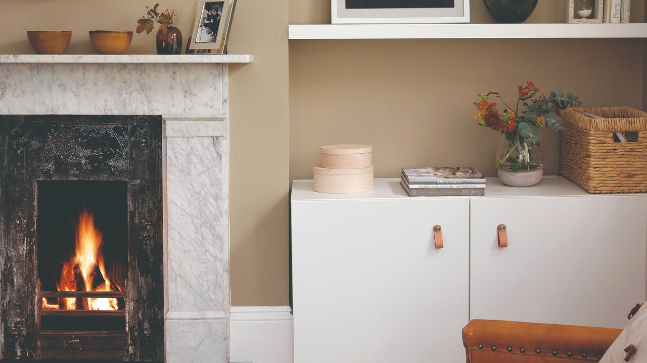 A beige-painted living room with a white IKEA BESTA cabinet next to a lit marble fireplace