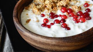 Wooden bowl with greek yogurt, cranberries and granola