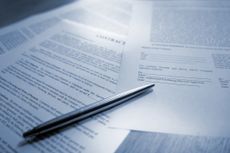 A blue tinted image of silver ball point pen lying on scattered legal contract documents on a wooden table, ready to sign to complete the deal. This conceptual image is shot with a shallow depth of field, and all paperwork is generic. Part of a contract series of images.