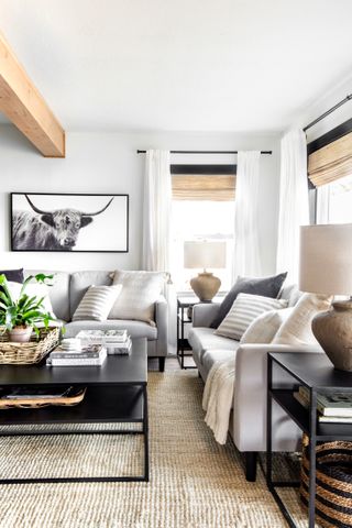 A white living room using neutral tones of beige and black, grey sofas and natural textures including woven baskets and linen lampshades