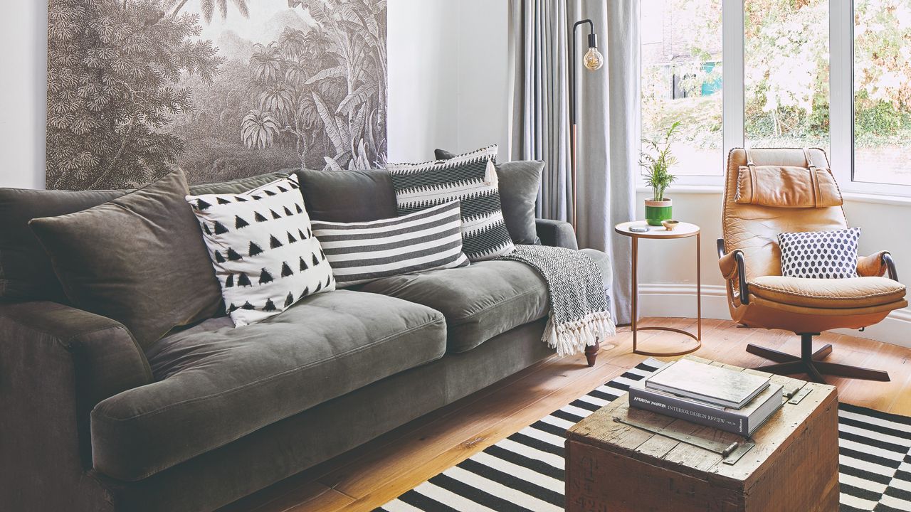 A living room with a dark grey velvet sofa, a brown leather swivel chair and a black and white striped rug